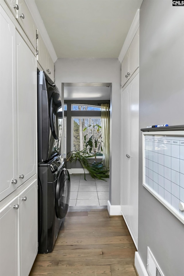 clothes washing area with stacked washer / drying machine, dark hardwood / wood-style floors, and cabinets