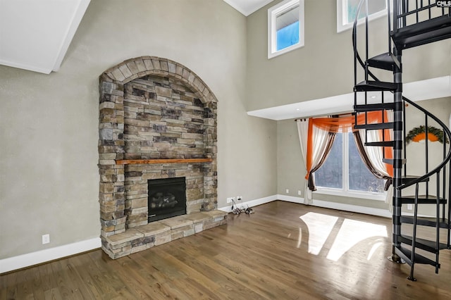 unfurnished living room featuring a fireplace, a towering ceiling, and wood-type flooring