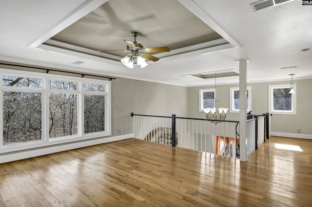 empty room with hardwood / wood-style floors, crown molding, ceiling fan with notable chandelier, and a raised ceiling