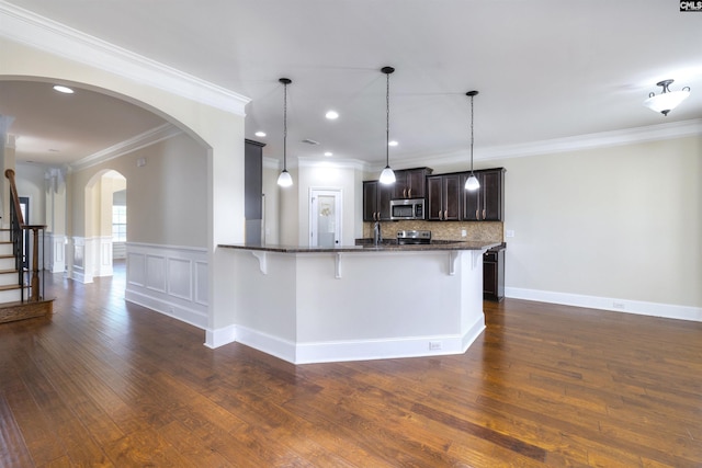 kitchen with appliances with stainless steel finishes, a breakfast bar, backsplash, hanging light fixtures, and dark brown cabinetry