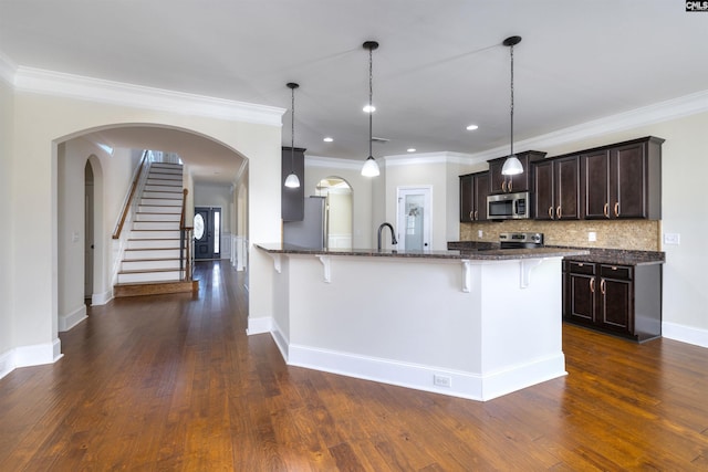 kitchen featuring a kitchen bar, hanging light fixtures, dark stone countertops, stainless steel appliances, and decorative backsplash