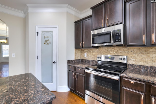 kitchen featuring crown molding, appliances with stainless steel finishes, dark brown cabinets, and dark stone counters