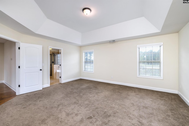 unfurnished bedroom featuring connected bathroom, a tray ceiling, and dark carpet