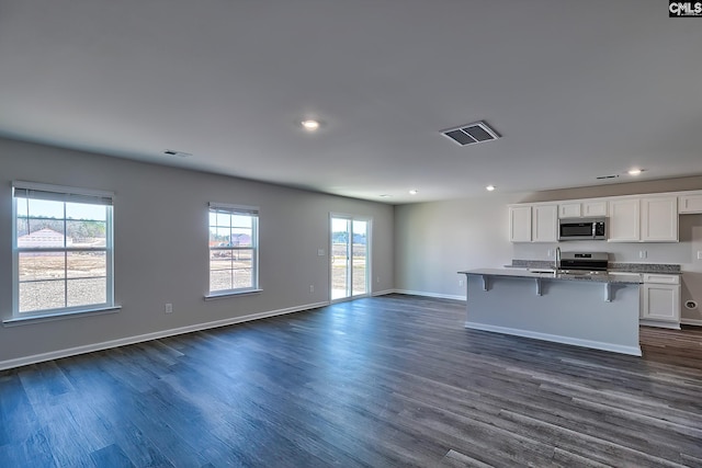 kitchen featuring appliances with stainless steel finishes, a breakfast bar, white cabinetry, dark hardwood / wood-style flooring, and a center island with sink