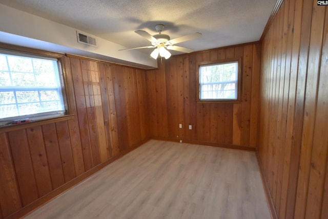 empty room with ceiling fan, a textured ceiling, light hardwood / wood-style floors, and a healthy amount of sunlight