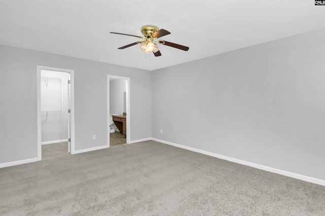 unfurnished bedroom with ensuite bath, a spacious closet, light colored carpet, a closet, and ceiling fan