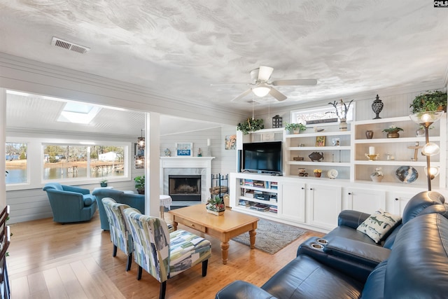 living room with a skylight, a high end fireplace, a wealth of natural light, and light hardwood / wood-style floors