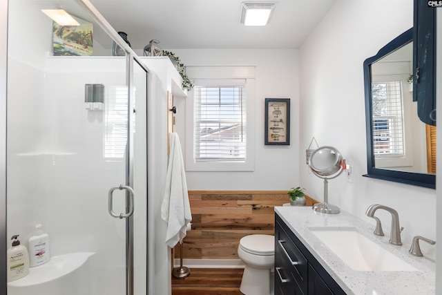 bathroom featuring hardwood / wood-style flooring, a shower with door, wooden walls, vanity, and toilet