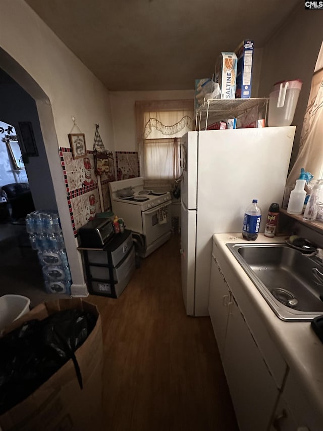 kitchen with arched walkways, white appliances, a sink, light countertops, and dark wood finished floors