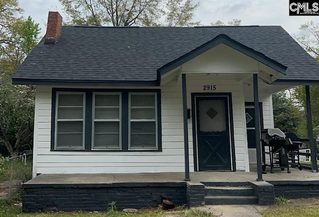 view of front of home with a chimney, a porch, and roof with shingles