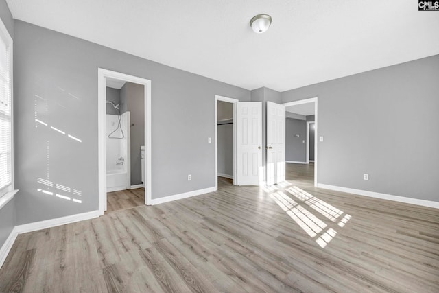 unfurnished bedroom featuring a walk in closet, light hardwood / wood-style floors, and ensuite bathroom