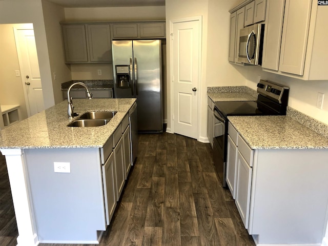 kitchen with sink, dark hardwood / wood-style flooring, stainless steel appliances, light stone countertops, and a kitchen island with sink