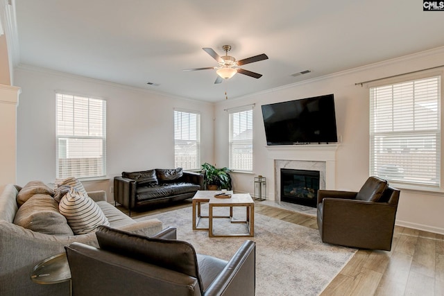 living room featuring a high end fireplace, ornamental molding, ceiling fan, and light wood-type flooring