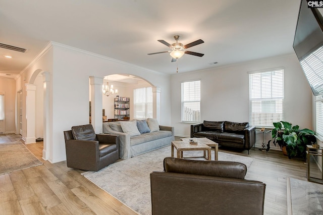 living room with ornate columns, ornamental molding, ceiling fan with notable chandelier, and light wood-type flooring