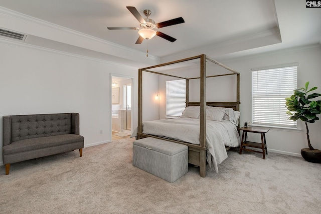 carpeted bedroom featuring a tray ceiling, connected bathroom, crown molding, and ceiling fan