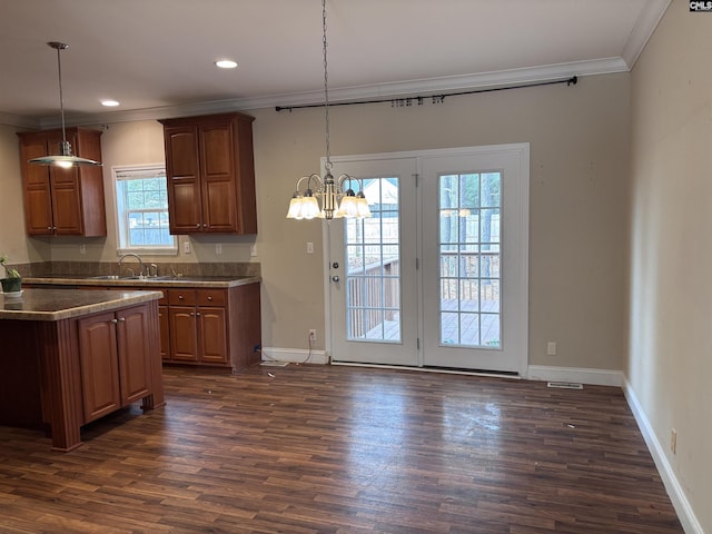 kitchen with hanging light fixtures, dark countertops, ornamental molding, and a sink