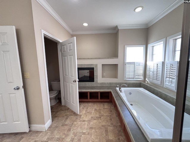 bathroom with toilet, baseboards, ornamental molding, a bath, and a tiled fireplace