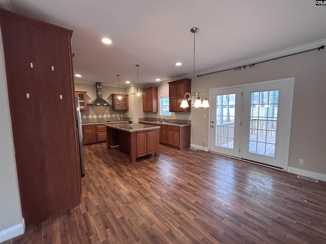 kitchen with a kitchen island, hanging light fixtures, wall chimney range hood, light countertops, and brown cabinetry