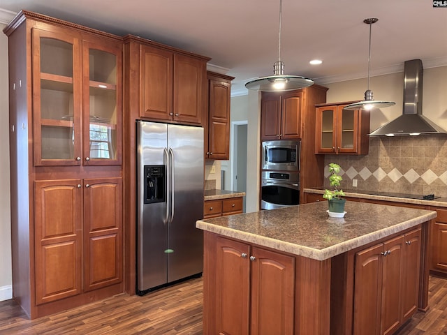 kitchen with appliances with stainless steel finishes, wall chimney range hood, a center island, glass insert cabinets, and pendant lighting