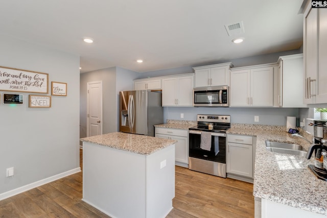 kitchen featuring stainless steel appliances, light stone countertops, a kitchen island, and white cabinets