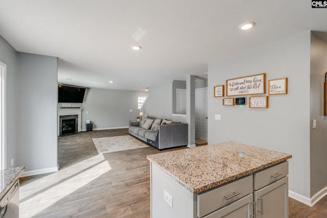 kitchen with dishwasher, light stone countertops, a center island, and hardwood / wood-style floors