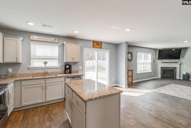 kitchen with dark hardwood / wood-style floors, white cabinetry, sink, a center island, and light stone countertops