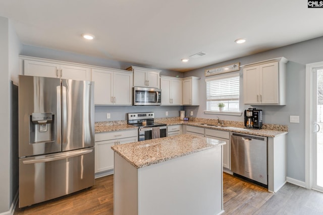 kitchen with a kitchen island, appliances with stainless steel finishes, white cabinetry, sink, and light stone counters