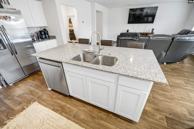 kitchen featuring sink, white cabinetry, light stone counters, a center island with sink, and stainless steel appliances