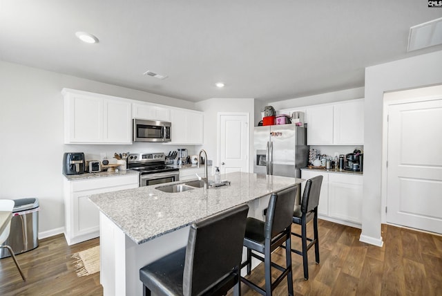 kitchen with a breakfast bar, white cabinetry, light stone counters, a center island with sink, and stainless steel appliances