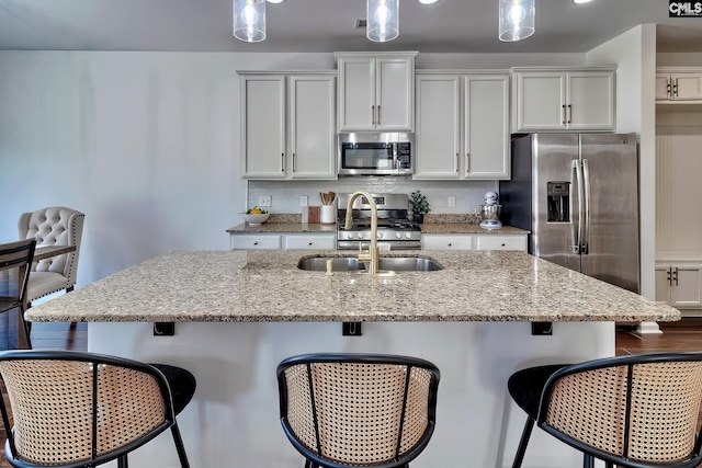 kitchen featuring pendant lighting, a kitchen island with sink, stainless steel appliances, a kitchen breakfast bar, and light stone counters