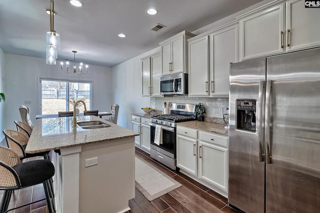 kitchen featuring sink, decorative light fixtures, appliances with stainless steel finishes, light stone countertops, and a kitchen island with sink