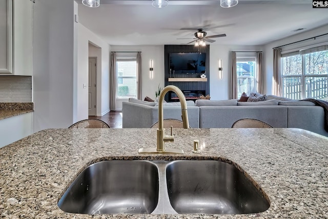 kitchen with sink, ceiling fan, tasteful backsplash, light stone countertops, and a large fireplace