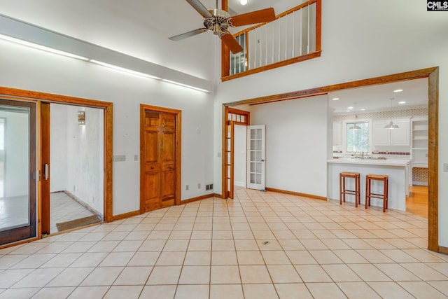 empty room featuring a high ceiling, light tile patterned flooring, ceiling fan, and french doors