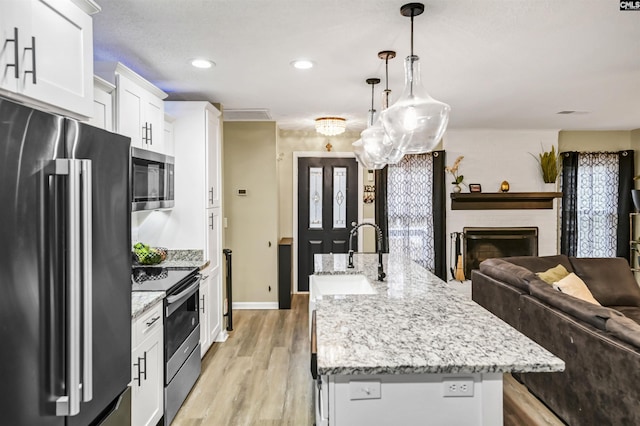 kitchen with appliances with stainless steel finishes, pendant lighting, white cabinetry, sink, and a center island with sink