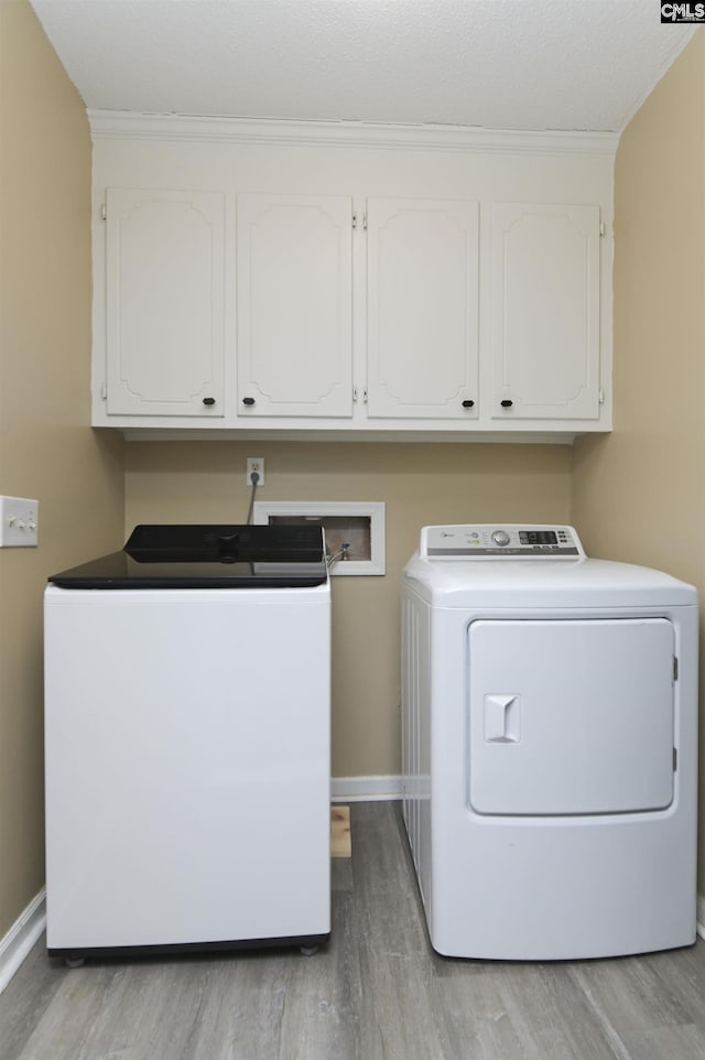 washroom featuring cabinets, ornamental molding, light hardwood / wood-style floors, and washer and dryer