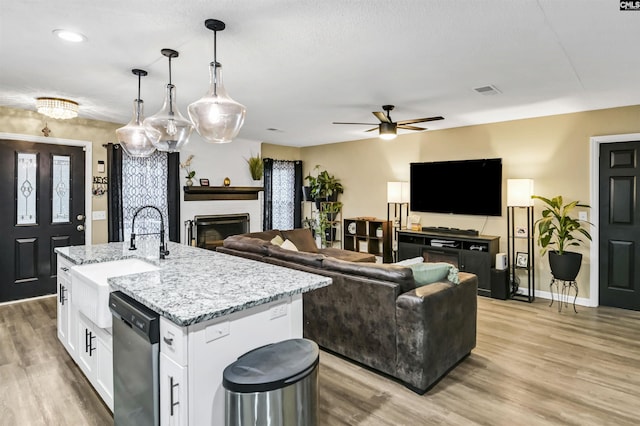 kitchen with sink, hanging light fixtures, a center island with sink, stainless steel dishwasher, and white cabinets