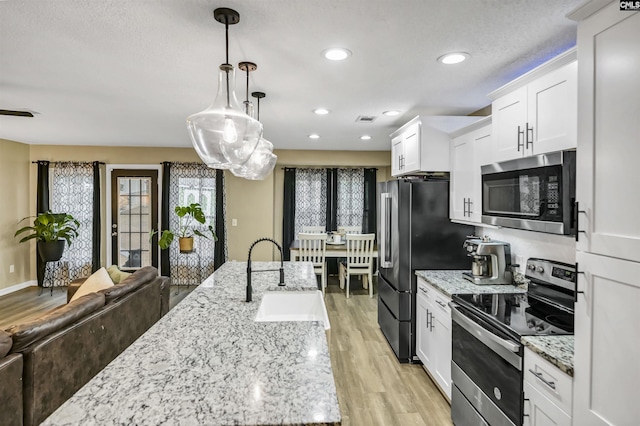 kitchen with pendant lighting, sink, light hardwood / wood-style flooring, white cabinetry, and stainless steel appliances