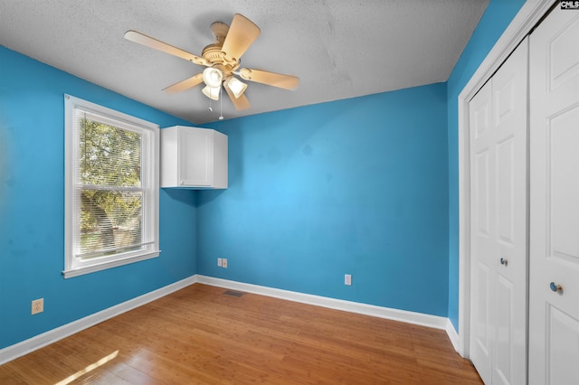 unfurnished bedroom with ceiling fan, a textured ceiling, light hardwood / wood-style floors, and a closet