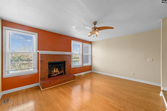 unfurnished living room with ceiling fan, a fireplace, a healthy amount of sunlight, and light wood-type flooring