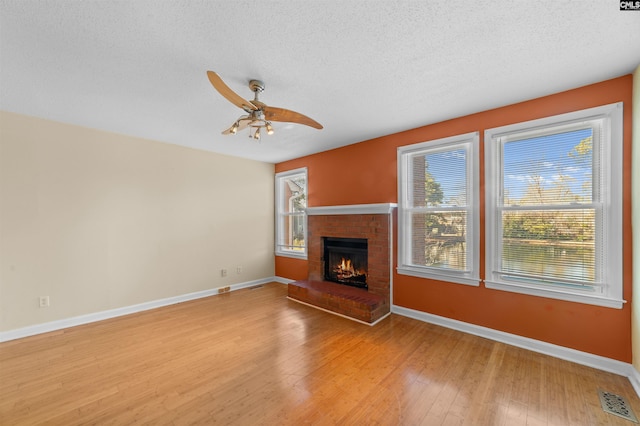 unfurnished living room featuring a brick fireplace, plenty of natural light, a textured ceiling, and light wood-type flooring