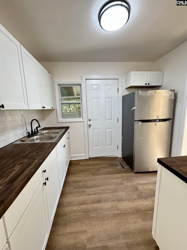 kitchen with sink, white cabinetry, tasteful backsplash, stainless steel fridge, and hardwood / wood-style floors