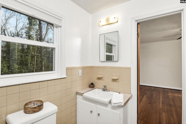 bathroom with wood-type flooring, tile walls, vanity, ceiling fan, and toilet