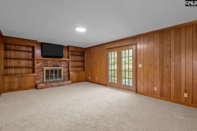 unfurnished living room featuring carpet, ornamental molding, a brick fireplace, french doors, and wood walls