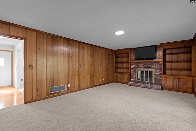 unfurnished living room with a brick fireplace, carpet floors, ornamental molding, and wood walls