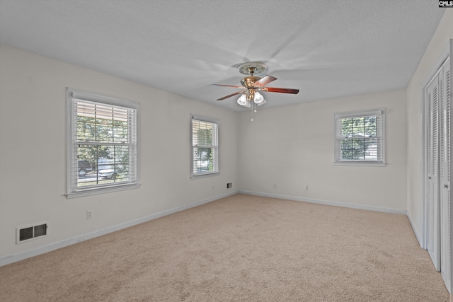 unfurnished bedroom featuring ceiling fan, light carpet, a textured ceiling, and a closet