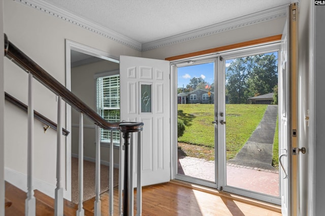 doorway featuring a healthy amount of sunlight, wood-type flooring, ornamental molding, and a textured ceiling