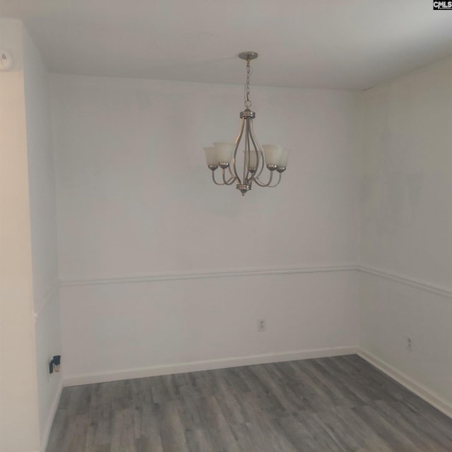 spare room featuring an inviting chandelier and dark wood-type flooring