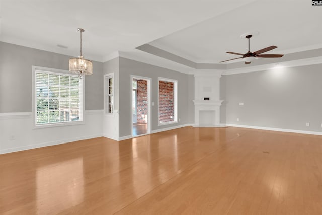 unfurnished living room with a raised ceiling, ornamental molding, ceiling fan with notable chandelier, and light hardwood / wood-style floors