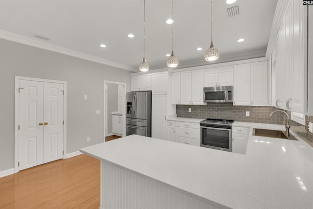 kitchen with decorative light fixtures, sink, white cabinets, ornamental molding, and stainless steel appliances