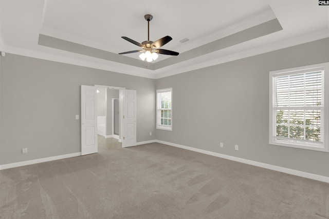 empty room with crown molding, a tray ceiling, light colored carpet, and ceiling fan